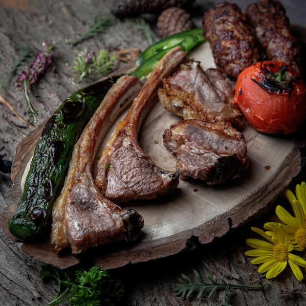 Close-up kebab costillas a la parrilla lula kebab con tomate al horno, pimienta en un plato de madera sobre una corteza de madera oscura