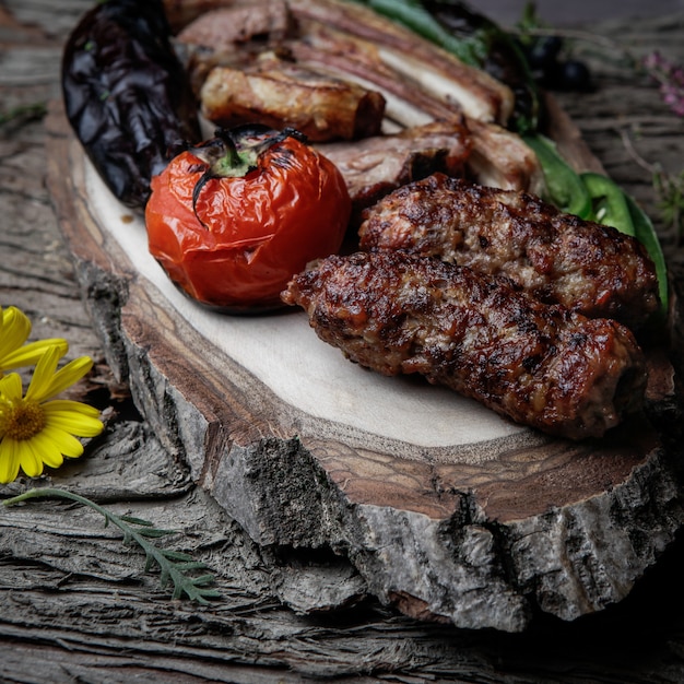 Close-up kebab costillas a la parrilla lula kebab con tomate al horno, pimiento y berenjenas en un plato de madera sobre una corteza de madera oscura