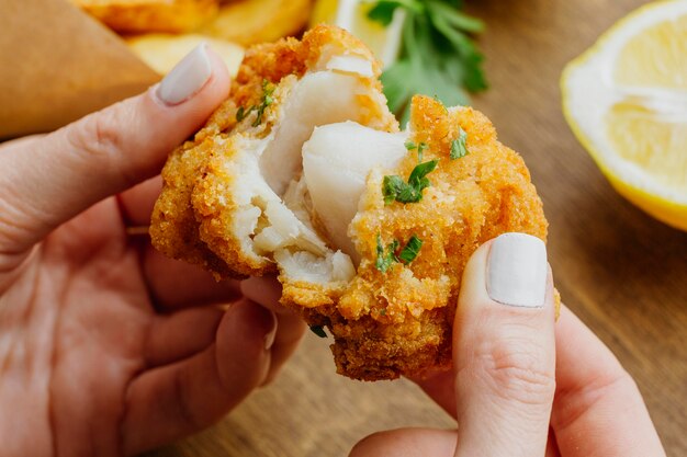 Close-up de mujer rompiendo un trozo de plato de pescado y patatas fritas