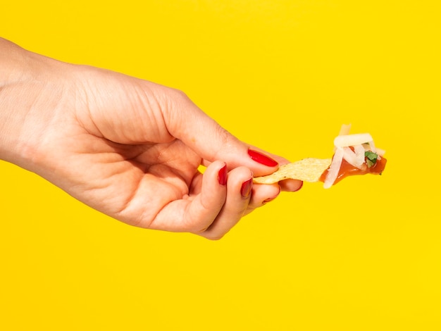 Close-up mujer sosteniendo chips de tortilla con fondo amarillo