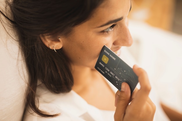 Close-up mujer sosteniendo una tarjeta de crédito junto a su mejilla