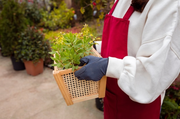 Close-up mujer vestida con ropa de jardinería y sosteniendo la cesta en invernadero