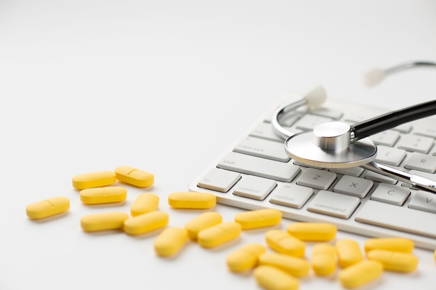 Close-up de pastillas amarillas y estetoscopio en el teclado sobre fondo blanco.
