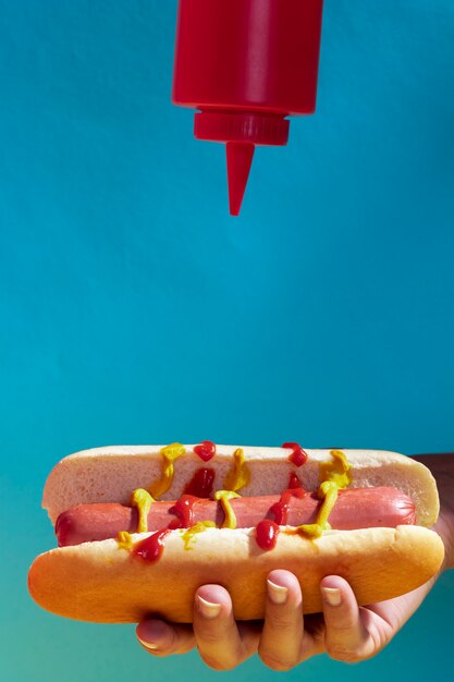 Close-up persona vertiendo salsa de tomate en hot dog