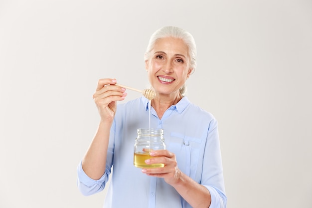 Close-up retrato de anciana sonriente, sosteniendo tarro de miel con cuchara