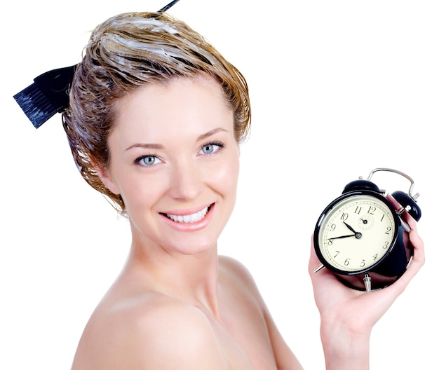 Close-up retrato de hermosa mujer joven con atractiva sonrisa coloreando el cabello y sosteniendo la alarma - aislado