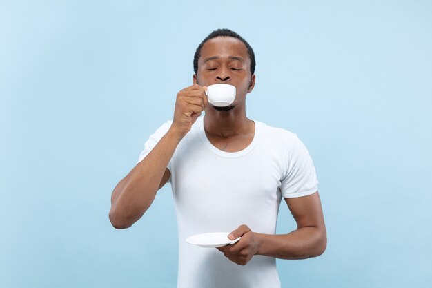 Close up retrato de joven afroamericano con camisa blanca. Disfrutando, tomando café, sonriendo.