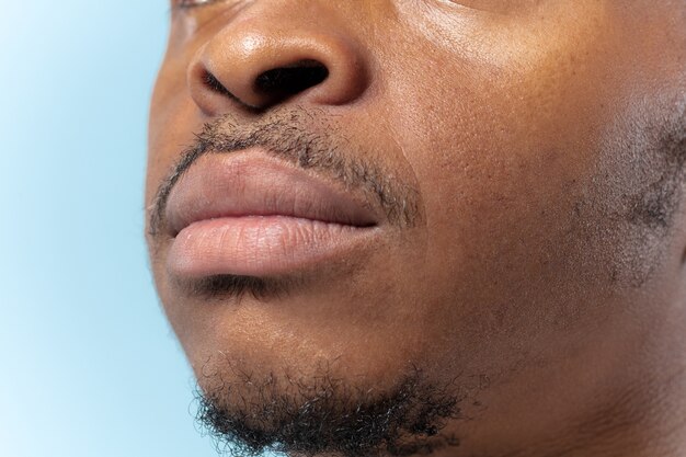 Close up retrato de joven afroamericano sobre fondo azul. Las emociones humanas, la expresión facial, la publicidad, las ventas o el concepto de salud y belleza de los hombres. Photoshot de labios. Parece tranquilo.