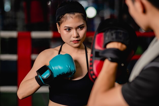 Close up retrato joven mujer bonita ejercicio con entrenador guapo en clase de boxeo y defensa personal en el ring de boxeo en el gimnasio, actuación de lucha femenina y masculina, enfoque selectivo y