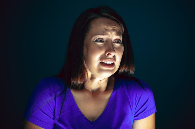 Close Up retrato de mujer joven loca asustada y conmocionada aislada en la oscuridad