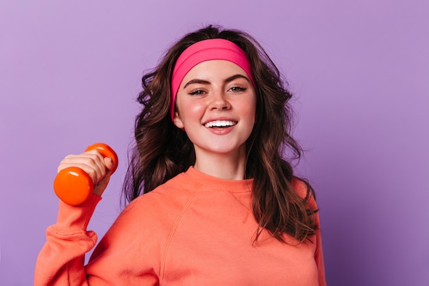 Close-up retrato de mujer rizada de ojos verdes en suéter naranja y diadema deportiva rosa