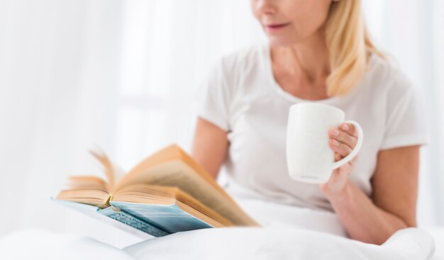 Close-up senior mujer leyendo un libro en la cama