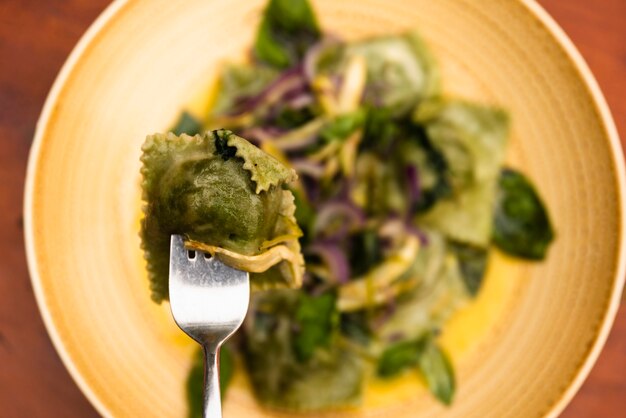 Close-up de tenedor con pasta de ravioles verdes en placa