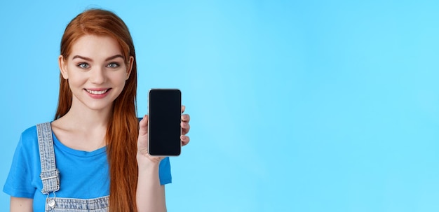 Foto gratuita closeup atractiva alegre pelirroja joven asistente de tienda femenina sugiere que el cliente compre el espectáculo del teléfono inteligente