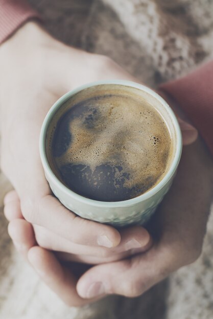 Closeup de café sabroso expreso con espuma de color amarillo sabroso en la taza de cerámica verde. Manos masculinas sosteniendo caliente bebida caliente.