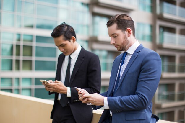 Closeup de dos colegas serios Texting al aire libre