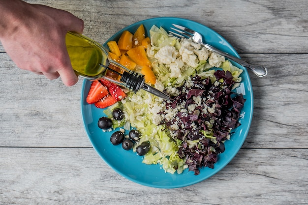 Closeup foto de una ensalada de verduras y frutas con una persona vertiendo aceite vegetal