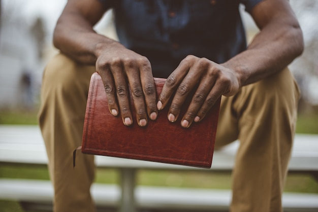 Closeup foto de un hombre sentado en el parque mientras sostiene la biblia