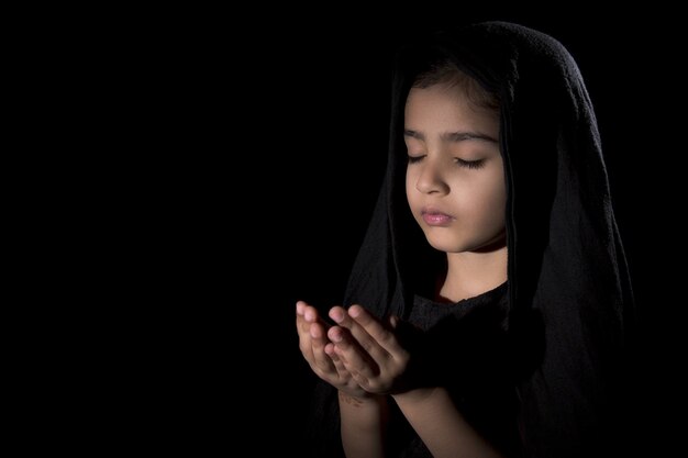 Closeup foto de una joven mujer rezando con los ojos cerrados en la pared negra