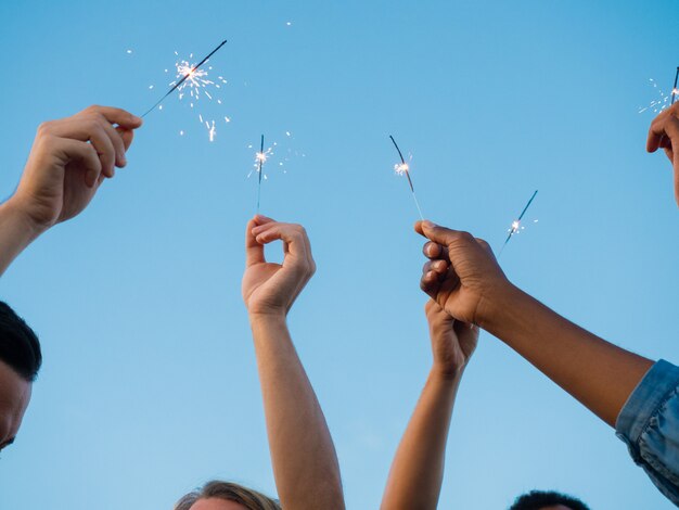 Closeup foto de jóvenes con luces de bengala en manos levantadas. Grupo de amigos divirtiéndose en la fiesta al aire libre. Concepto de celebración