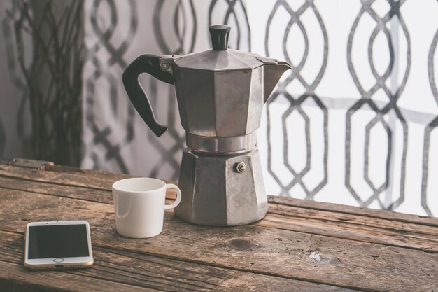 Closeup foto de un teléfono inteligente con una taza blanca y una tetera gris sobre una superficie de madera