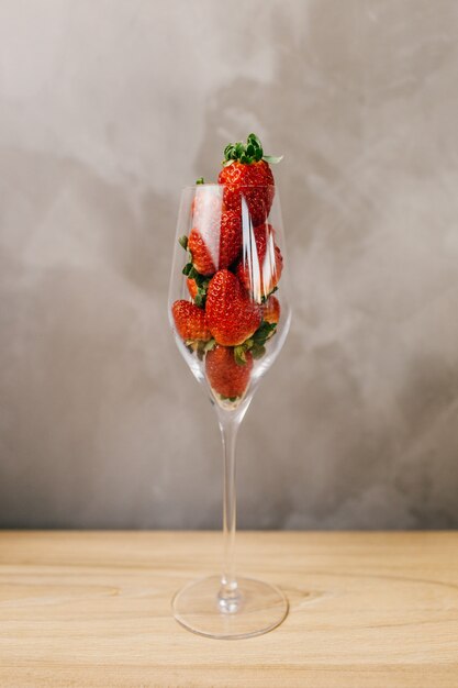 Closeup foto de un vaso lleno de fresas enteras delante de una pared gris