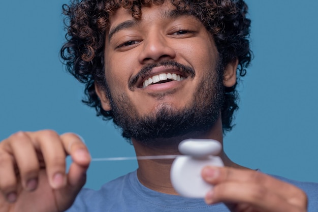 Closeup retrato de un alegre chico indio sosteniendo el contenedor de hilo dental abierto en sus manos