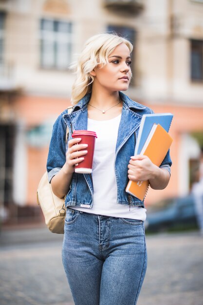 Closeup retrato de estudiante rubia sonriente con un montón de cuadernos vestidos con jeans