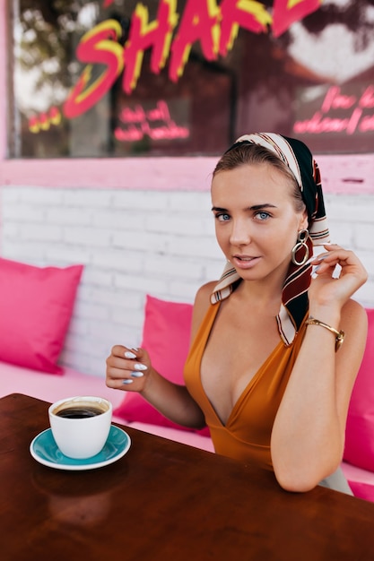 Closeup retrato de feliz modelo de mujer rubia lleva joyas y accesorios para la cabeza bebiendo café fuera