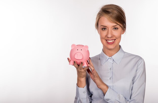 Closeup retrato feliz, sonriente mujer de negocios, la celebración de hucha rosa, aislado en el interior de oficina de fondo. Ahorro presupuestario financiero, concepto de inversión inteligente