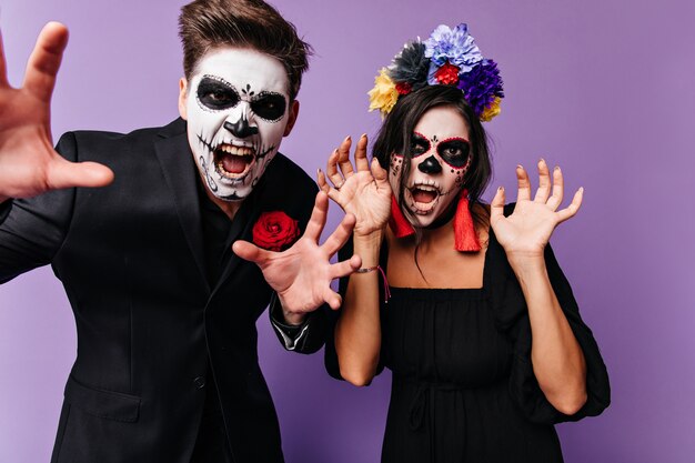 Closeup retrato en Halloween de hombre y mujer posando con caras aterradoras. Pareja en ropa negra con detalles rojos gritando.