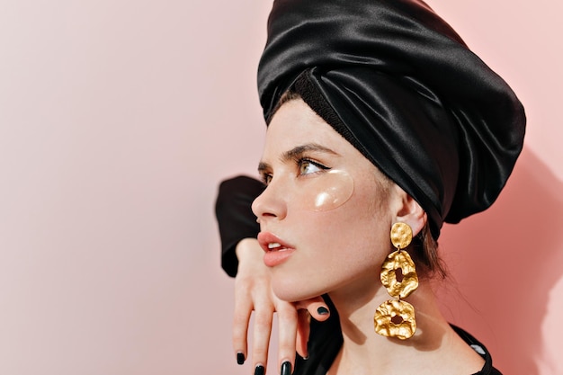 Closeup retrato de hermosa mujer joven con grandes aretes de oro usando parches en los ojos Chica europea pensativa posando en turbante