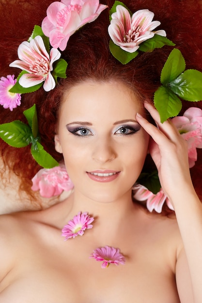 Closeup retrato de la hermosa mujer pelirroja jengibre sonriente cara con coloridas flores en el pelo tocando la cara