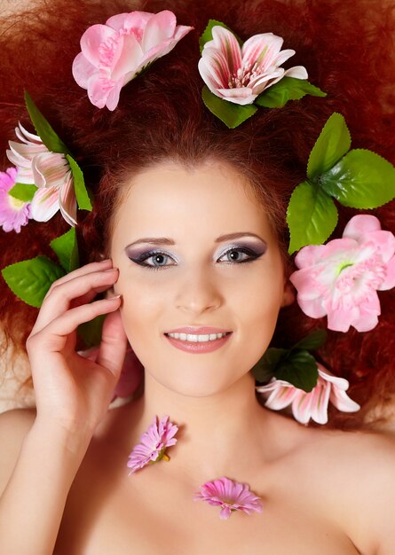 Closeup retrato de la hermosa mujer pelirroja jengibre sonriente cara con coloridas flores en el pelo tocando la cara