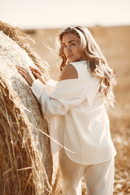 Closeup retrato de hermosa mujer sonriente. La rubia sobre un fardo de heno. Un campo de trigo en el fondo.
