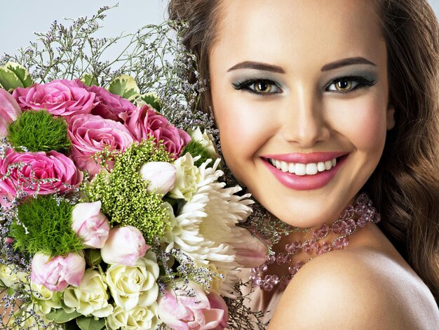 Closeup retrato de hermosa niña feliz con flores en las manos. Mujer atractiva joven sostiene el ramo de flores de primavera
