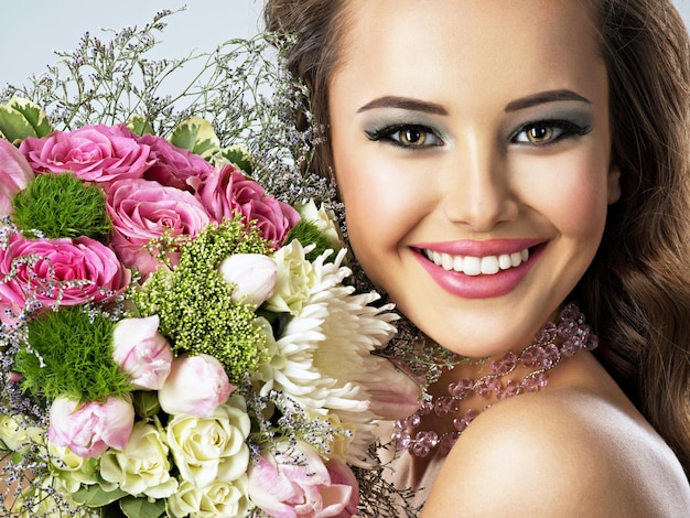 Closeup retrato de hermosa niña feliz con flores en las manos. Mujer atractiva joven sostiene el ramo de flores de primavera