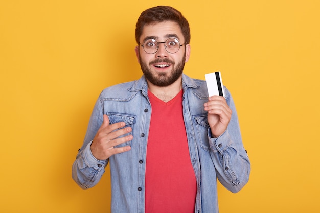 Closeup retrato de hombre barbudo asombrado con tarjeta de crédito en las manos, se ve emocionado, descubrió una gran cantidad de dinero en la tarjeta