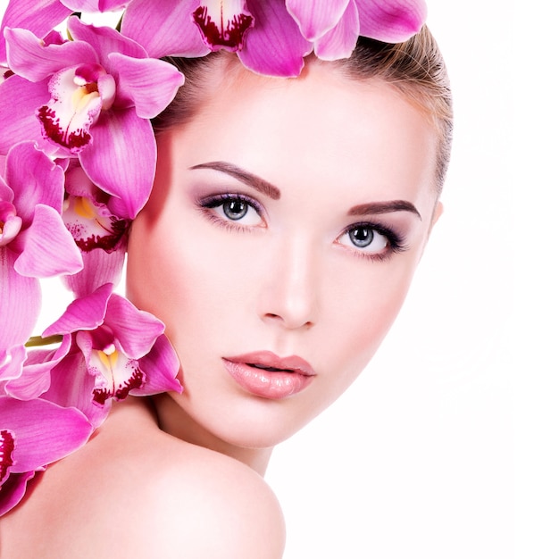 Closeup retrato de joven bella mujer con una piel limpia y sana de la cara. Chica bastante adulta con flor cerca de la cara. - aislado en fondo blanco