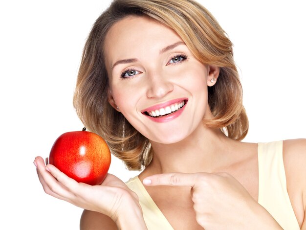 Closeup retrato de una joven y bella mujer sonriente apuntando con el dedo a la manzana aislada en blanco.