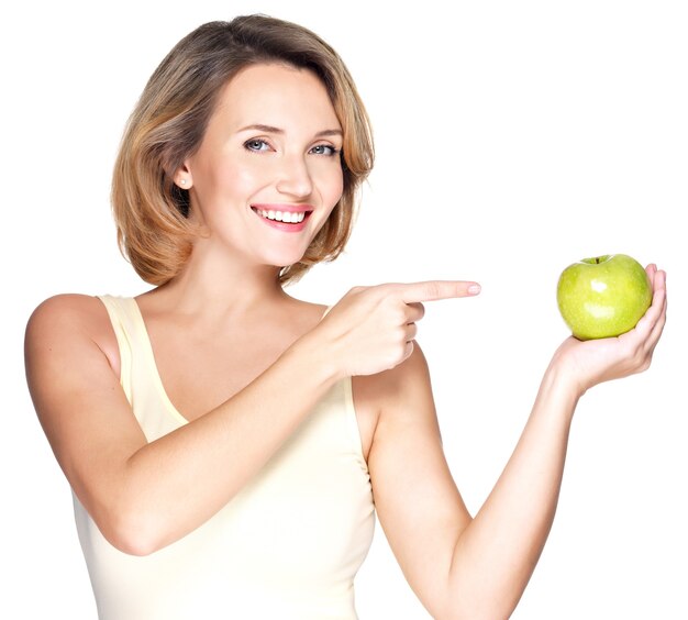 Closeup retrato de una joven y bella mujer sonriente apuntando con el dedo a la manzana aislada en blanco.