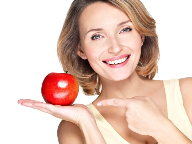 Closeup retrato de una joven y bella mujer sonriente apuntando con el dedo a la manzana aislada en blanco.