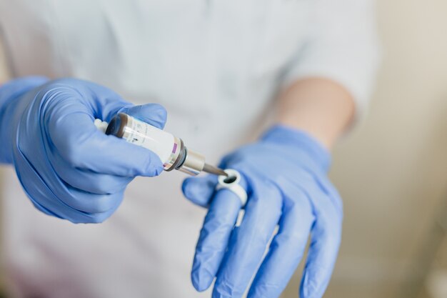 Closeup retrato de las manos del doctor en guantes azules que trabajan con la medicina moderna. Procedimientos dermatológicos profesionales, lifting, rejuvenecimiento, gotas, asistencia sanitaria