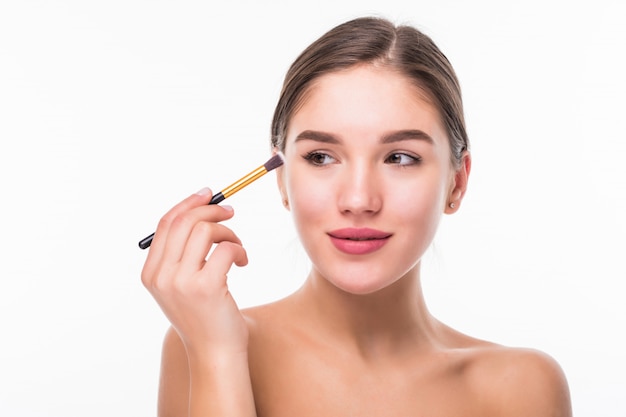 Closeup retrato de una mujer aplicando base tonal cosmética seca en la cara con pincel de maquillaje aislado en la pared blanca