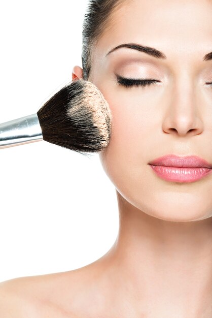 Closeup retrato de una mujer aplicando base tonal cosmética seca en la cara con pincel de maquillaje.
