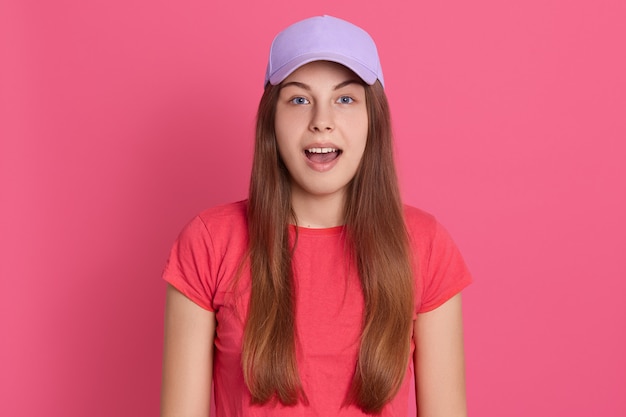 Closeup retrato de mujer asombrada vistiendo camiseta roja y gorra de béisbol, mantiene la boca abierta, se ve sorprendido