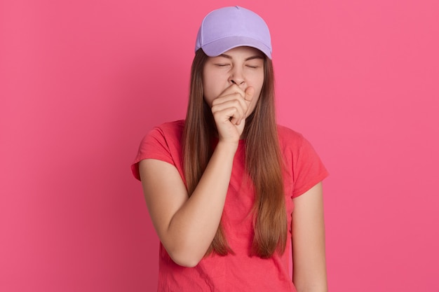 Closeup retrato de mujer cansada bostezando cubriendo su boca con el puño, se ve exhausto, vistiendo camiseta y gorra de béisbol,