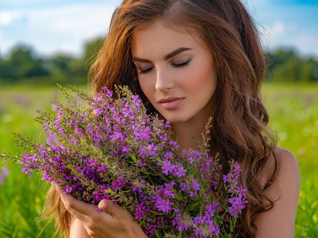 Closeup retrato de una mujer caucásica relajante en la naturaleza. Mujer joven al aire libre con un ramo. Chica en un campo con flores de lavanda en sus manos.