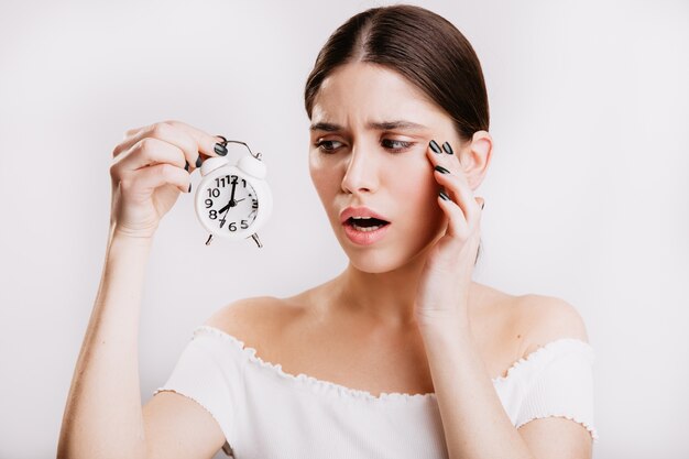 Closeup retrato de mujer europea emocionada en pared aislada. Chica mira tristemente el reloj blanco.