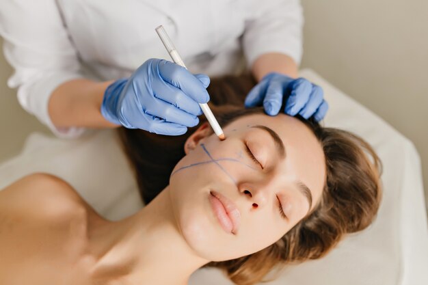Closeup retrato de mujer hermosa durante la preparación para la terapia de cosmetología en salón de belleza. Procedimientos dermatológicos profesionales, lifting, rejuvenecimiento.